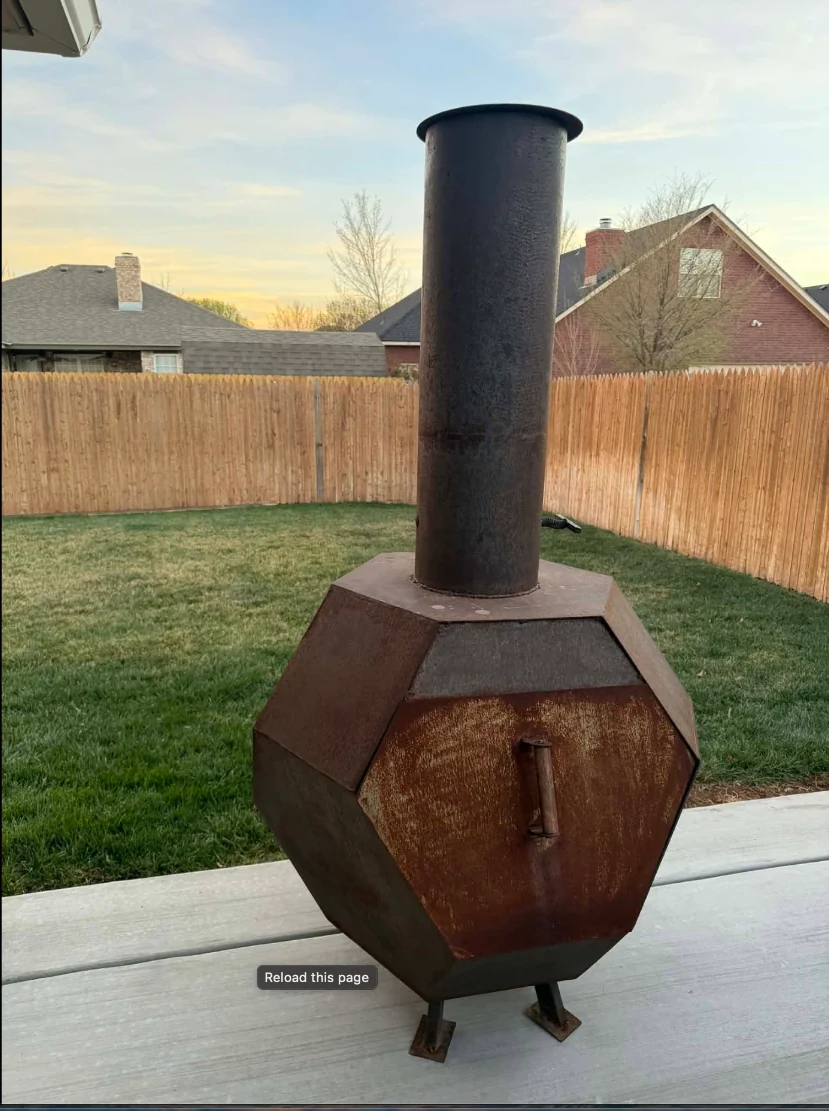 Tall geometric steel chimney fire pit standing on a patio with a wood fence behind it